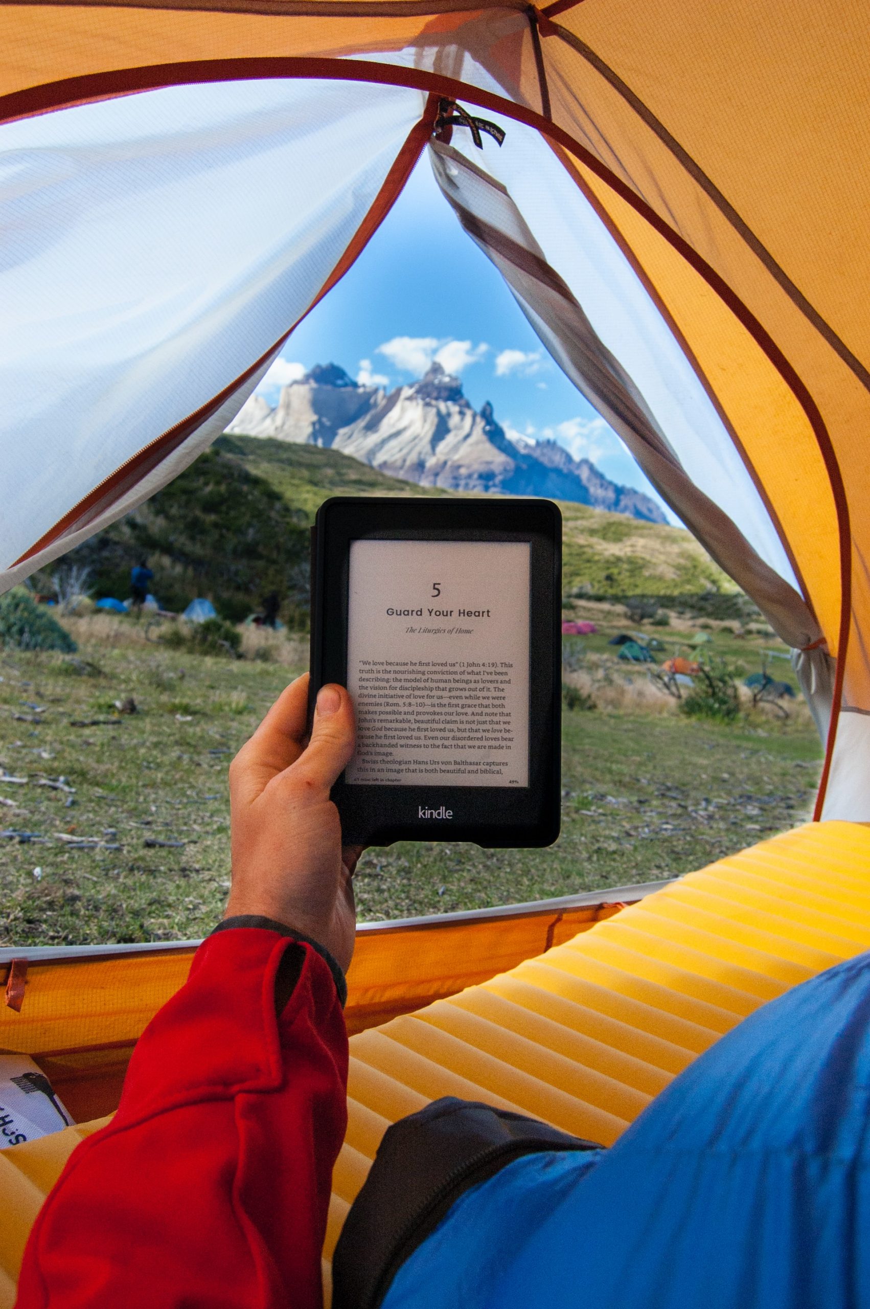 Male hand holding ebook, inside tent with view of mountains in background